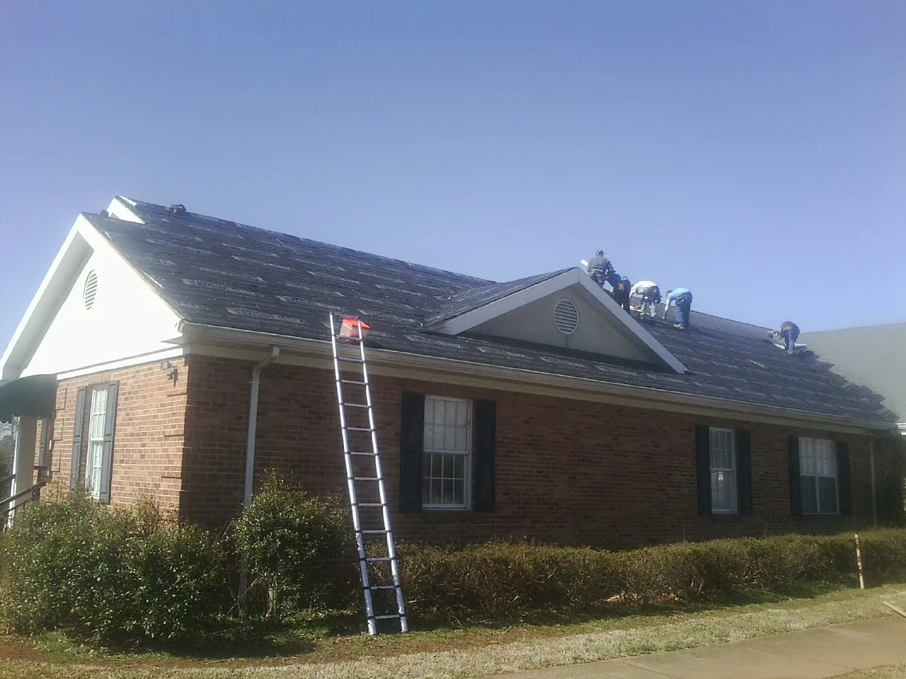 Crew tearing shingles off a brick ranch roof with a ladder set — Emergency Roof Repair work by our crew in Knob Lick