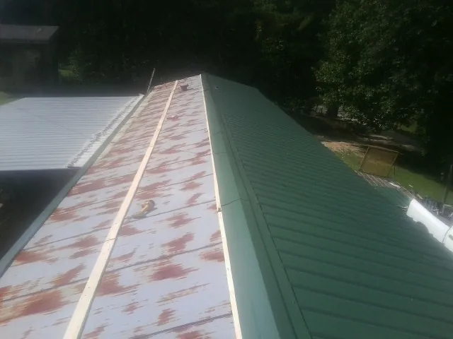 Old rusted panels beside newly installed green metal roofing — Wind Damage Roof Repair by Roofing Brothers in Knob Lick