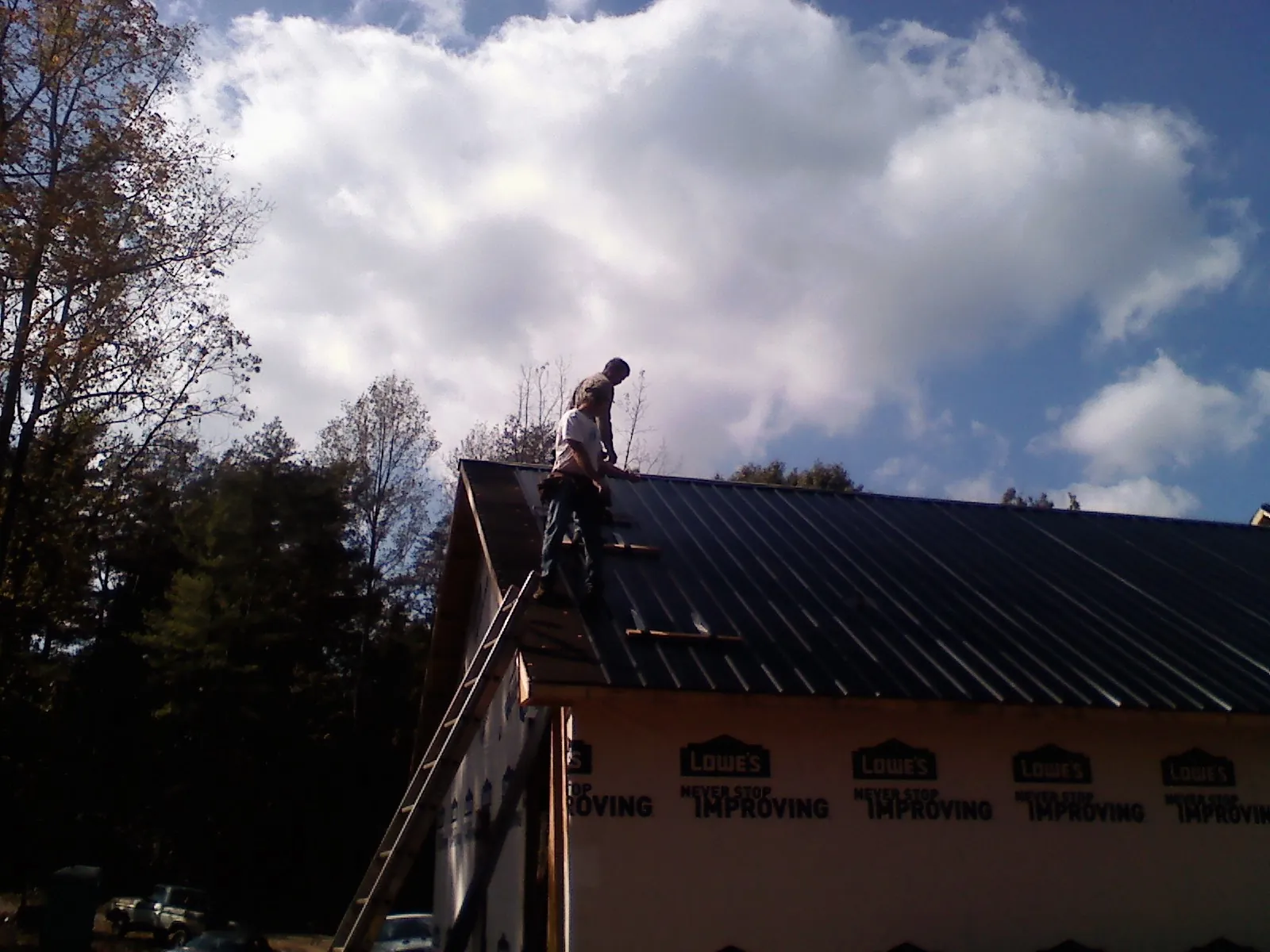 Roofer fastening dark metal panels high against a cloudy sky, from a Roof Inspection job in Knob Lick
