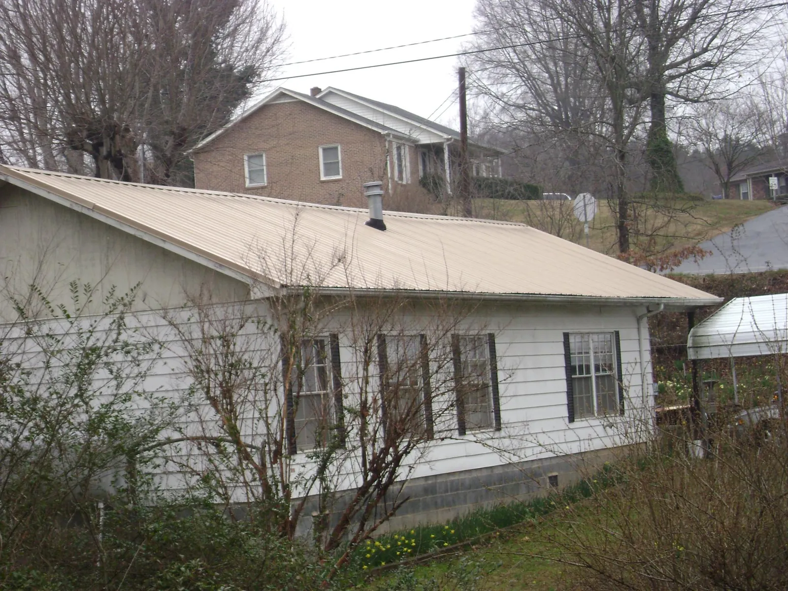 Tan metal roof on a white sided house set into a hillside — Commercial Roofing by Roofing Brothers in Knob Lick